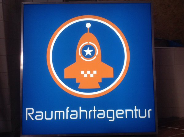 Logo of the Raumfahrtagentur, an orange rocket with a blue star in the midle in a circle.